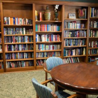 A cozy library room with wooden bookshelves filled with books and a round table surrounded by chairs.