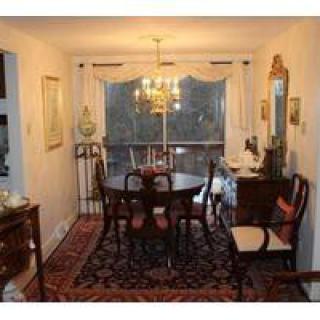 A classic dining room with a dark wood table and chairs, an ornate chandelier, and decorative elements like a mirror and curtains.
