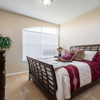 A cozy bedroom with a wooden bed frame, decorated with red and white bedding, featuring a large window and a dresser.