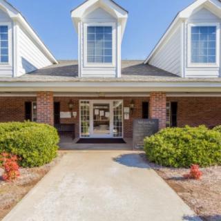A welcoming front entrance of a brick residential building with manicured bushes and a clear pathway.