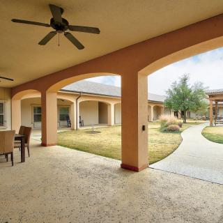 A serene outdoor patio area with a ceiling fan, seating, and a view of the landscaped courtyard.