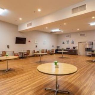 A spacious dining area with round tables and chairs, featuring a wooden floor and soft lighting.