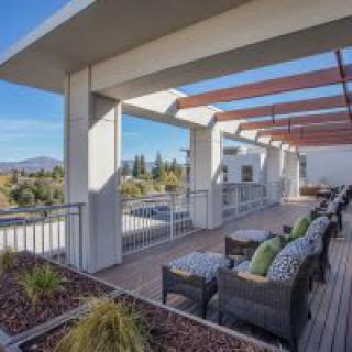 A spacious outdoor patio with seating under a modern pergola, overlooking a scenic landscape.