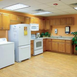 A modern kitchen and laundry space featuring wooden cabinets, a refrigerator, an oven, a microwave, and a washing machine.