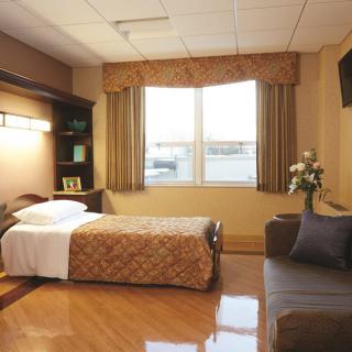 A tidy and well-lit hospital room with a single bed, sofa, and a window view.