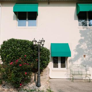 A house with green awnings over the windows and door, surrounded by a garden with bushes and flowers.