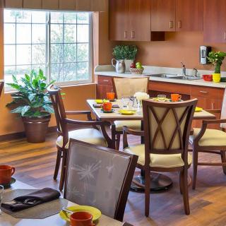 A cozy kitchen and dining area with wooden furniture and plants near a large window.