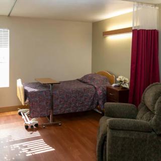 A hospital room with a single bed, recliner chair, and privacy curtain under natural light.