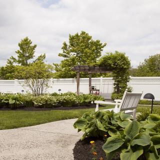 A serene backyard garden with lush greenery, a white fence, and comfortable outdoor seating.
