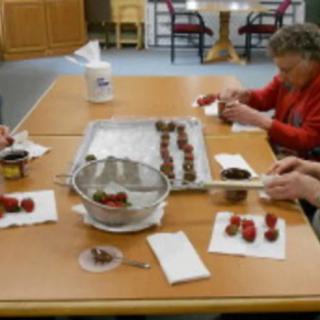 Elderly individuals engaged in a group baking activity, preparing desserts on a table.
