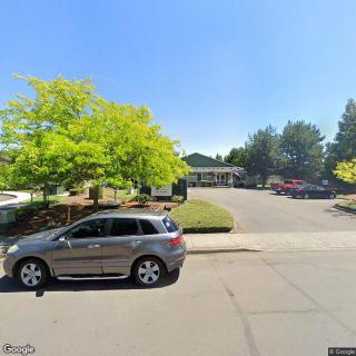 A parked car on a sunny day in front of a building and parking lot with trees.