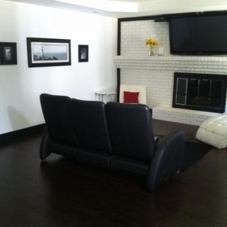 A modern and minimalist living room with a black sofa, white walls, dark flooring, and a fireplace, featuring a wall-mounted television and artwork.