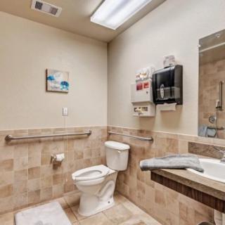 A clean and accessible bathroom featuring a toilet, sink, hand dryer, and grab bars.