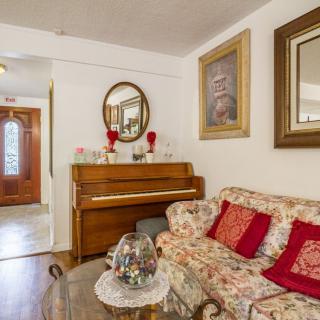 A cozy living room featuring a piano, floral upholstered couch with red cushions, and decorative elements including artwork and a mirror.