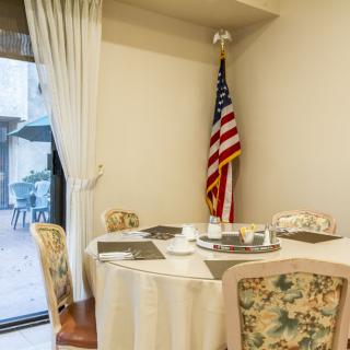 A cozy dining area with a round table and floral chairs, featuring an American flag in the corner.