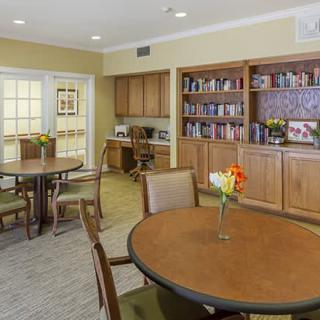 A cozy reading area with bookshelves, tables, and chairs in a well-lit room.