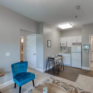 A cozy living space with a view of the kitchen, featuring a blue chair and dining table.