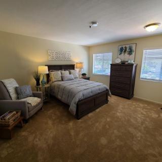 A cozy bedroom with a neatly made bed, an armchair, and a dresser.
