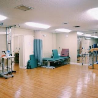 A rehabilitation and physical therapy room equipped with exercise machines and treatment tables.