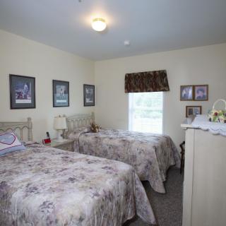 A cozy bedroom with twin beds, decorated with framed pictures and a window providing natural light.