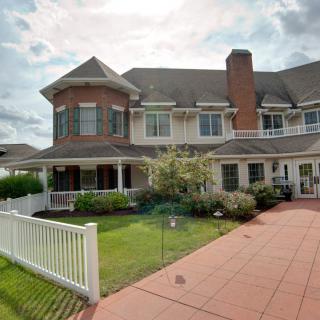 A large, two-story brick and wood house with a spacious front yard and white picket fence.