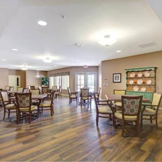 A spacious and well-lit dining room with several tables and chairs arranged on wooden flooring.