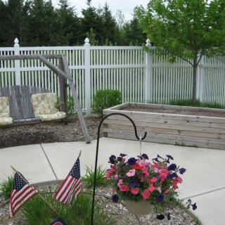A peaceful garden patio with a swing, a flower pot adorned with small flags, and a white fence in the background.