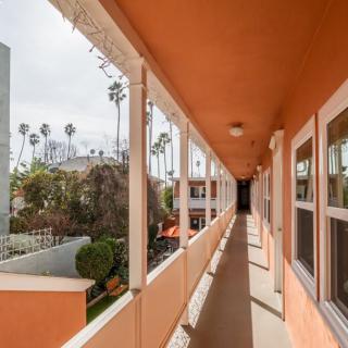 A view down an exterior corridor of a vibrant orange apartment complex with palm trees in the background.
