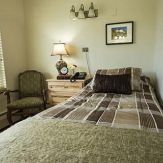 A cozy bedroom with a bed, side table, lamp, and a chair.