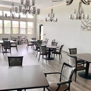 An empty dining room with several tables and chairs, illuminated by multiple chandeliers.
