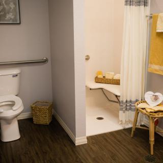 A modern bathroom featuring a toilet, shower area with a seat, and neatly arranged towels.
