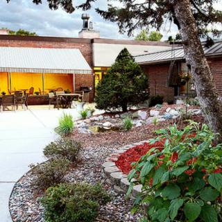 A beautifully landscaped garden with a patio area adjoining a brick building in the evening light.