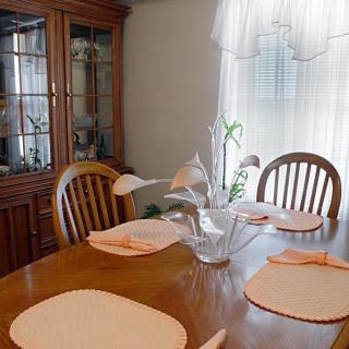 A cozy dining room with a wooden table set for four, featuring placemats and a vase with flowers.