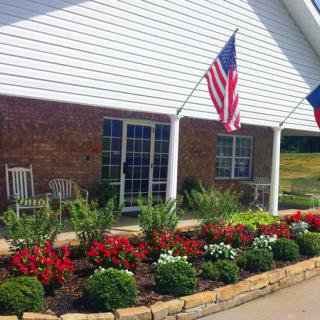 A house with a neatly landscaped garden featuring colorful flowers, patio chairs, and two flags displayed.