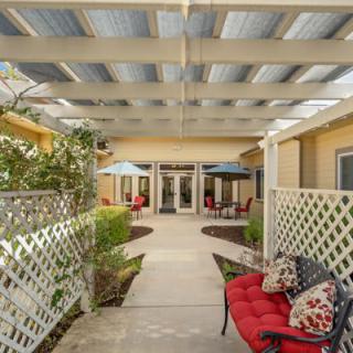A cozy outdoor patio with a pergola, featuring cushioned seating and surrounded by garden landscaping.