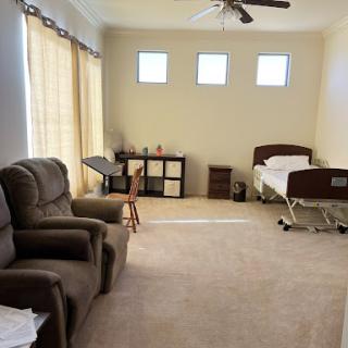 A cozy room featuring two recliner chairs, a bed, and a small table illuminated by natural light from the windows.