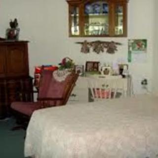 A cozy bedroom with a bed, chair, cabinet, and various decorative items.