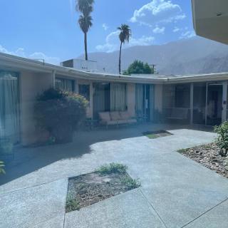A serene courtyard surrounded by a modern building, featuring palm trees and a clear sky.