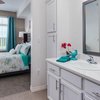 A modern bedroom with an adjoining bathroom featuring white cabinets and turquoise accents.