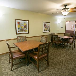 A cozy dining area featuring wooden tables and chairs, decorative artwork on the walls, and a carpeted floor.
