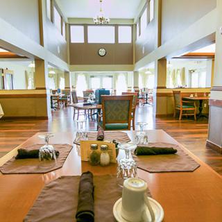 A spacious dining hall with neatly arranged tables and chairs, featuring a wooden floor and large windows.