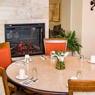 A cozy dining area with a round table set for four, featuring orange cushioned chairs and a fireplace in the background.