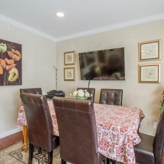 A cozy dining room featuring a floral tablecloth, leather chairs, wall art, and a mounted television.