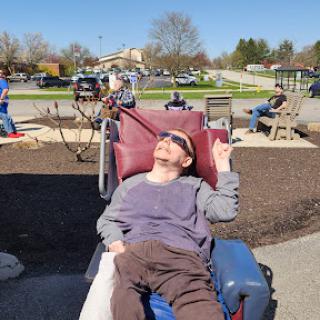 A person enjoying the sunny day in a park, relaxing on a comfortable chair.