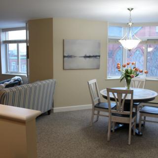 A cozy living and dining area with modern decor, featuring a round dining table, chairs, and a comfortable sofa surrounded by bright natural light.