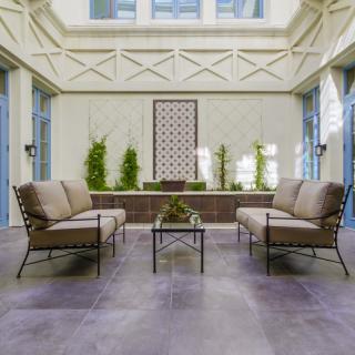 A modern outdoor patio with comfortable sofas and a coffee table, surrounded by plants.
