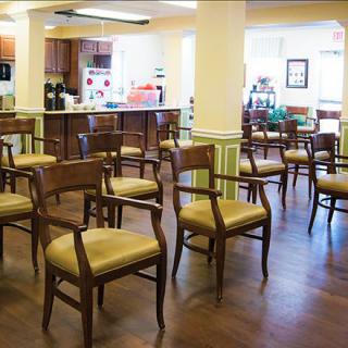 A brightly lit community room with several chairs arranged in a circle, adjacent to a kitchen area.