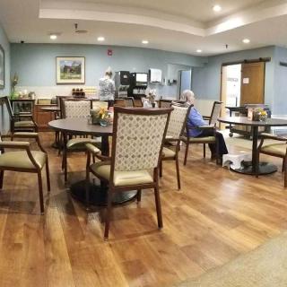 A dining area in a nursing home with tables, chairs, and a few elderly residents.