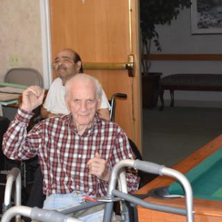 An elderly man in a wheelchair joyfully raises his hand while participating in a social activity.