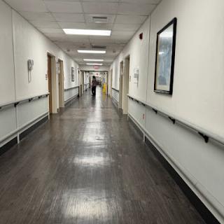 A long, empty hallway in a hospital with white walls and polished flooring.